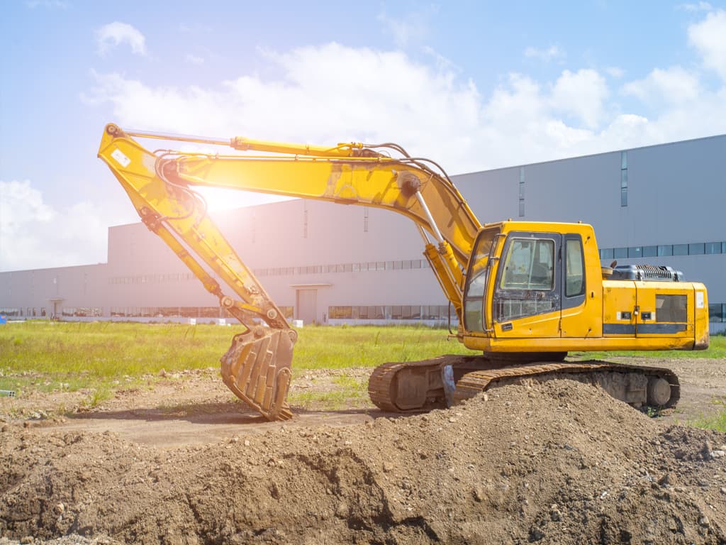 Excavator propriu pe șantier industrial, lângă hală